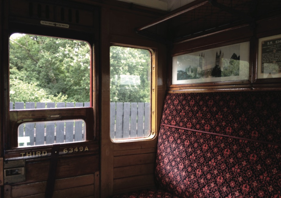 Interior view of a vintage third-class railway carriage showing patterned red upholstery and wooden panelling