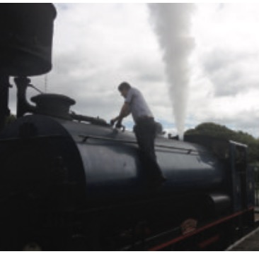 Worker preparing a steam locomotive, enveloped in white steam